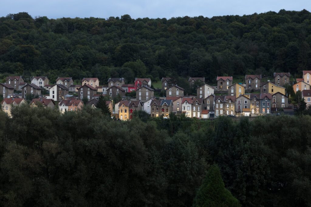 A group of row houses illuminated at dusk along the side of a hill in Longwy, France.