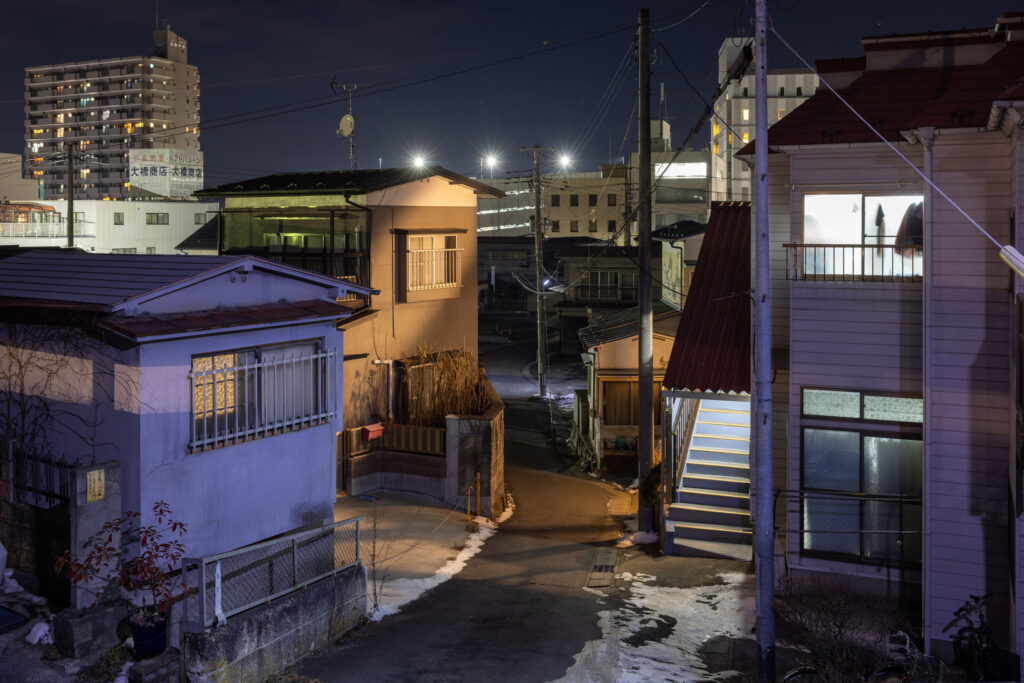 A cluster of homes at night, with snow on the ground.