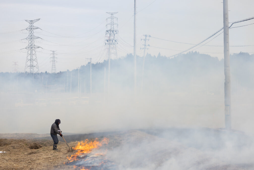A person works the edge of a controlled burn, surrounded by utility poles.