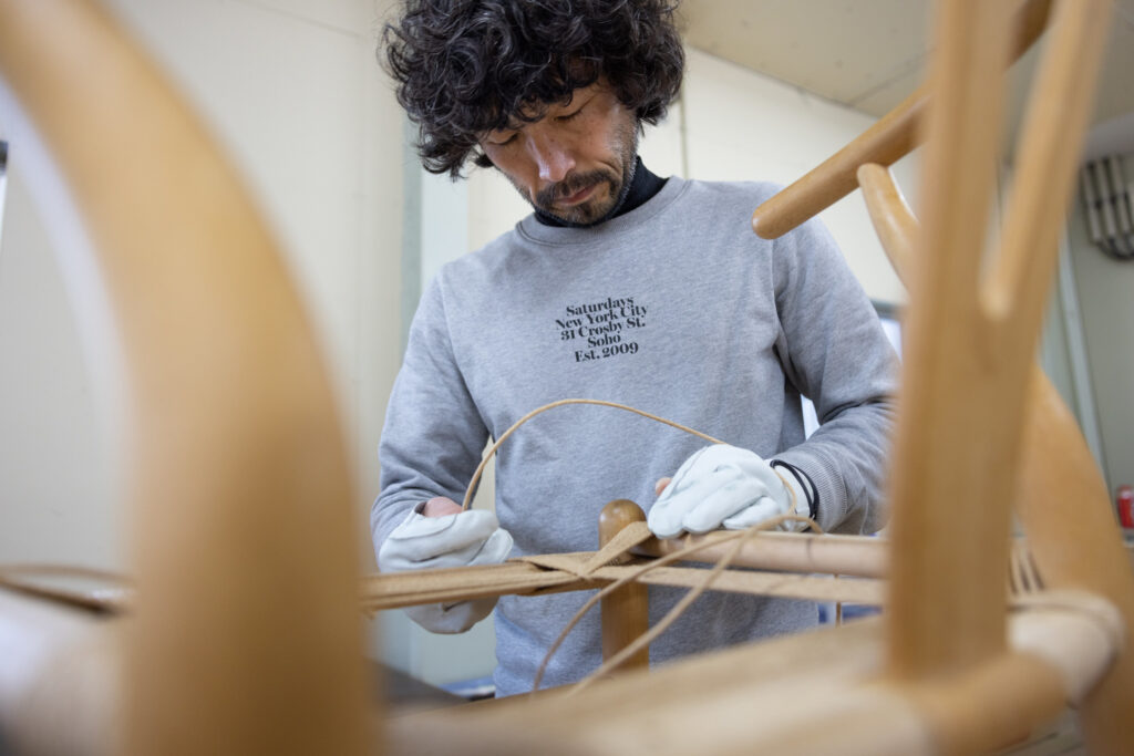 A person working carefully on a Carl Hansen CH24 Wishbone Chair, wearing gloves and focused on the task.