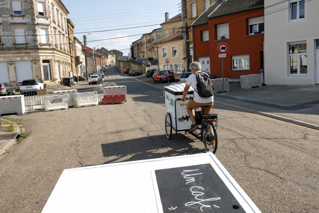 The view from a mobile coffee cart biking through a French town square, with another person riding another cart ahead.