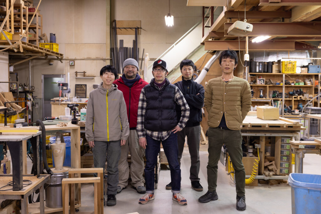 A group of five people standing in a workshop at Ishinomaki Laboratory, surrounded by tools.