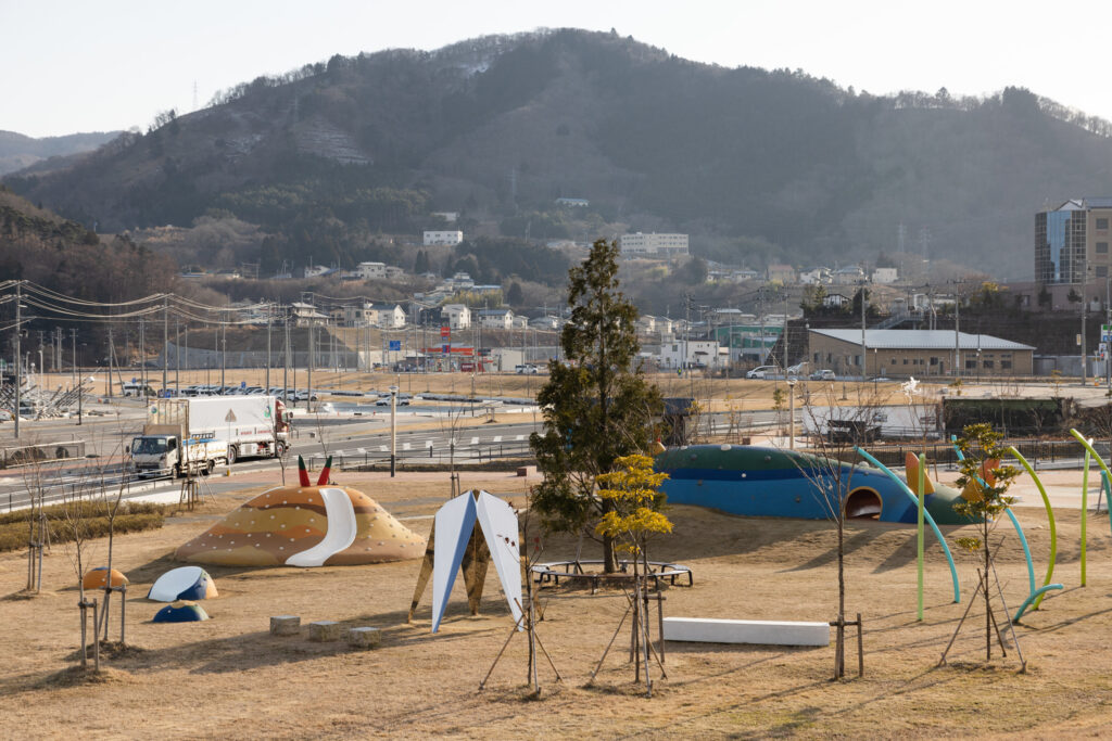 A view of a playground in T?hoku, Japan, featuring colorful, whimsical structures and a backdrop of hills and buildings.