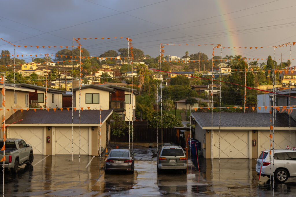 A photograph of flags strung between white poles, illustrating the shape of a proposed building. A rainbow is in the background.