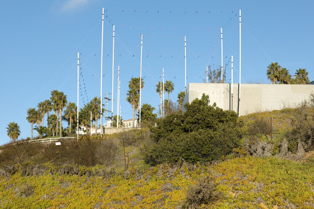 A photograph of a green and yellow hill with flags strung between white poles, illustrating the shape of a proposed building.