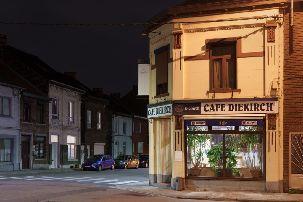 A photograph of Cafe Diekirch, a plant filled cafe, as seen from the street at night.