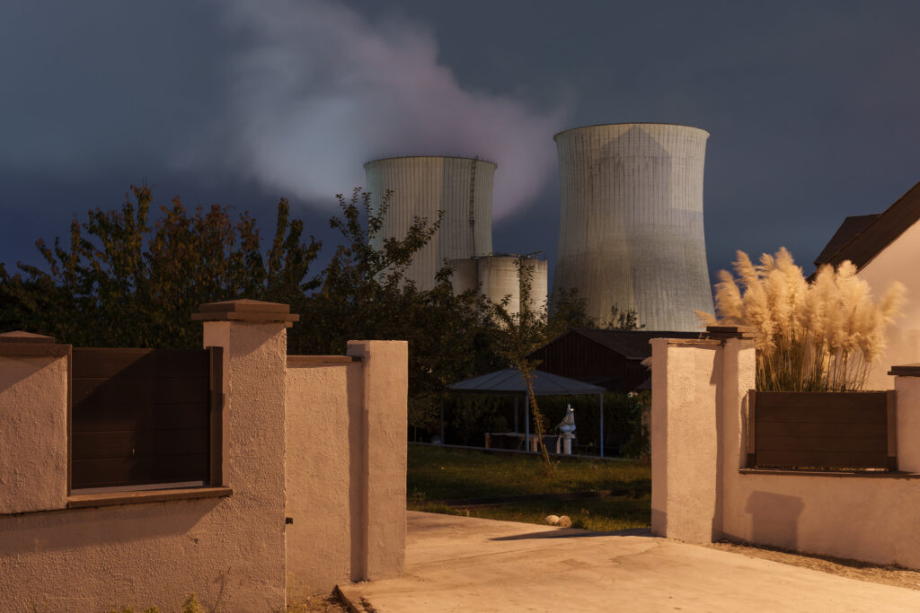 A photograph of two power plant cooling towers with a home wall in front at night.