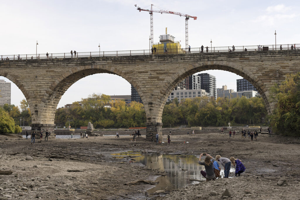 A family on the dry bed of the Mississippi River, with the Stone Arch Bridge in the mid ground.