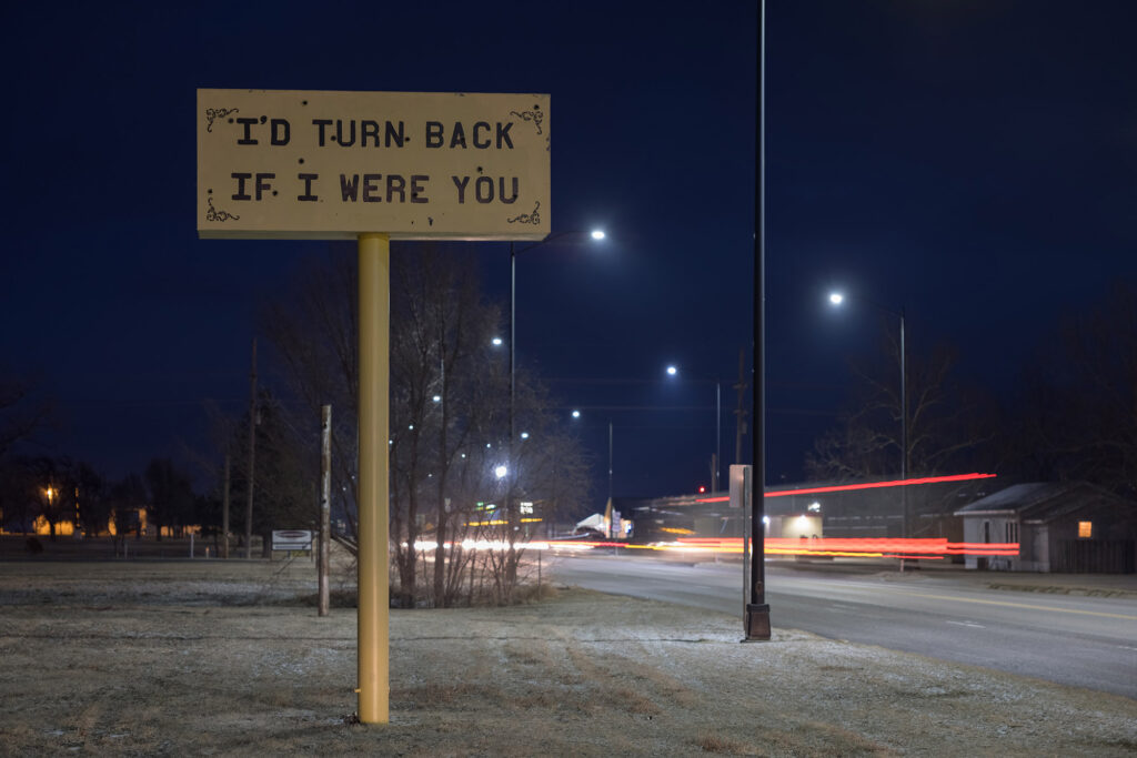 A sign that says "I'd turn back if I were you" in a winter, night landscape.