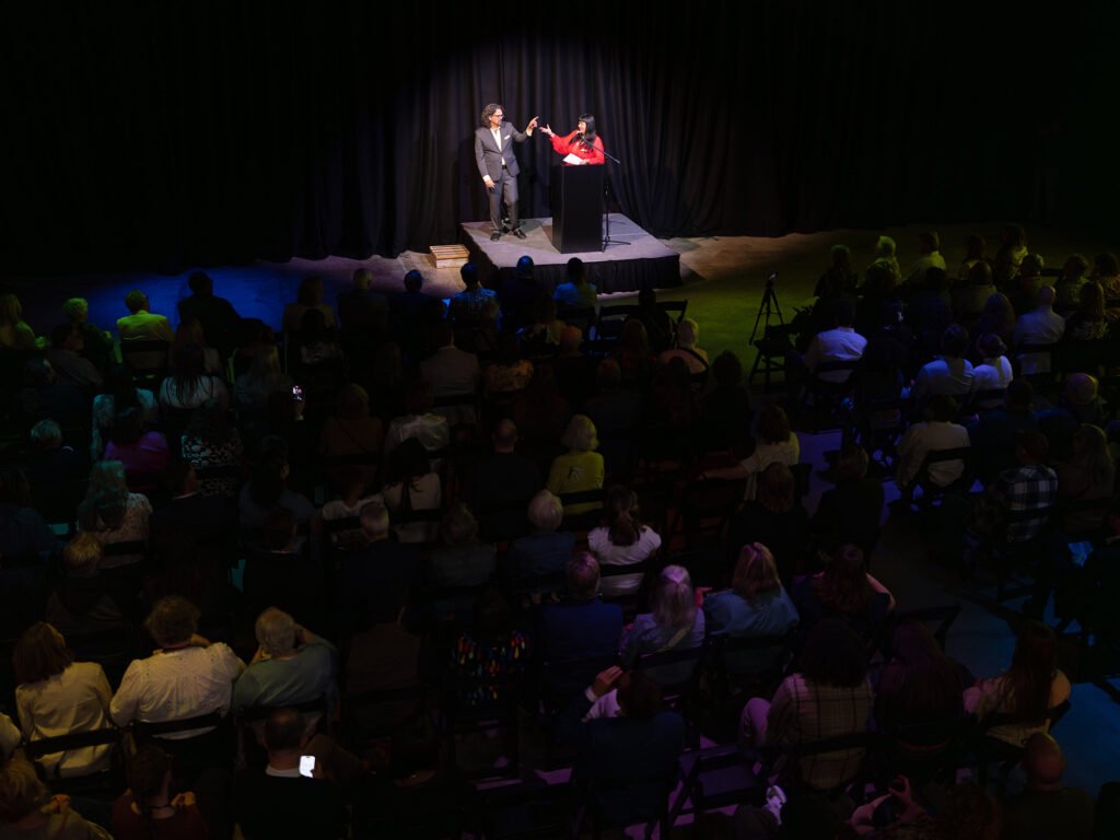 Two people are on a small stage in a large, dark room.