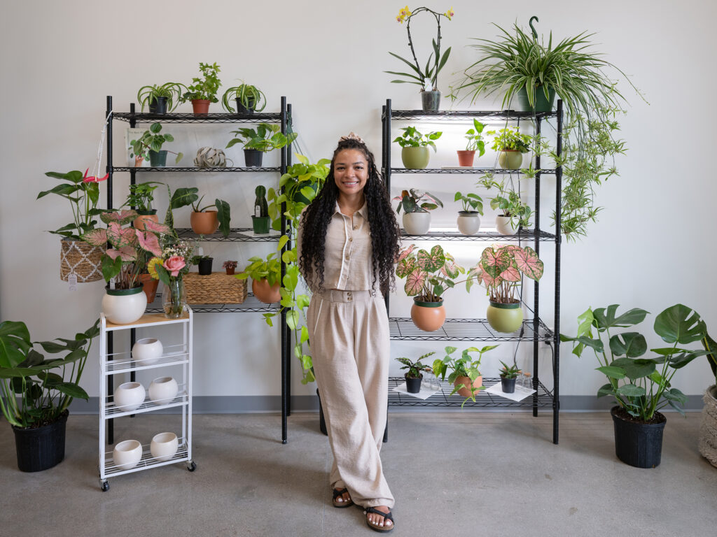 A woman stands in a room with plants behind her.